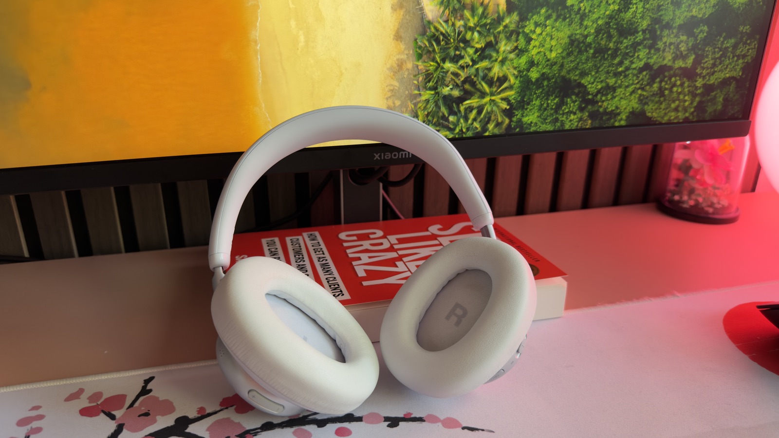 JBL Live 780NC i vitt stående på ett skrivbord framför en datorskärm